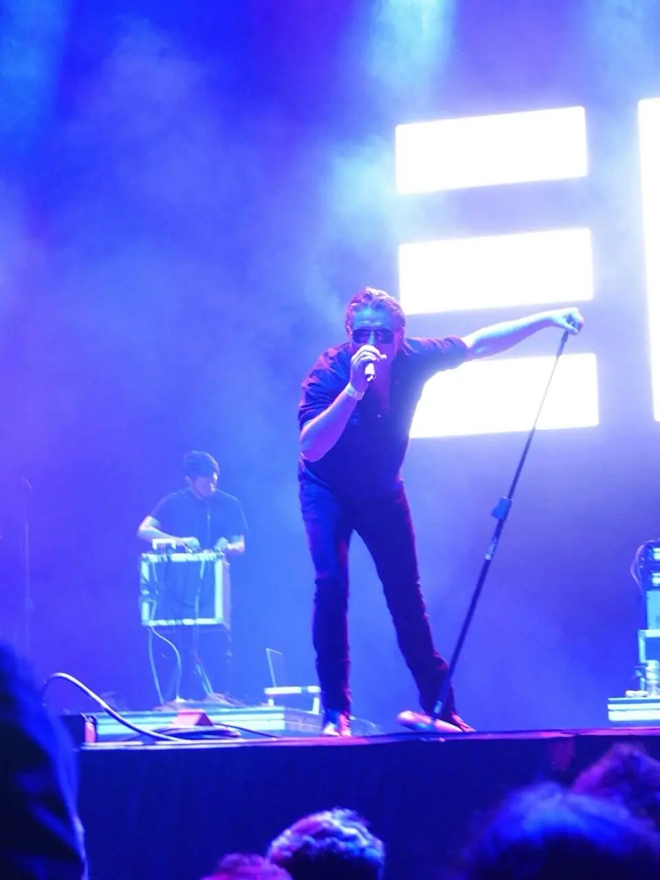 Black Line live in Mexico City: Douglas J. McCarthy singing in blue light, Cyrus at his rig behind, the band’s mark lit up