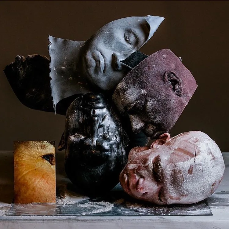 A still life of cast heads and faces piled on a table, pale, dark and flesh-coloured