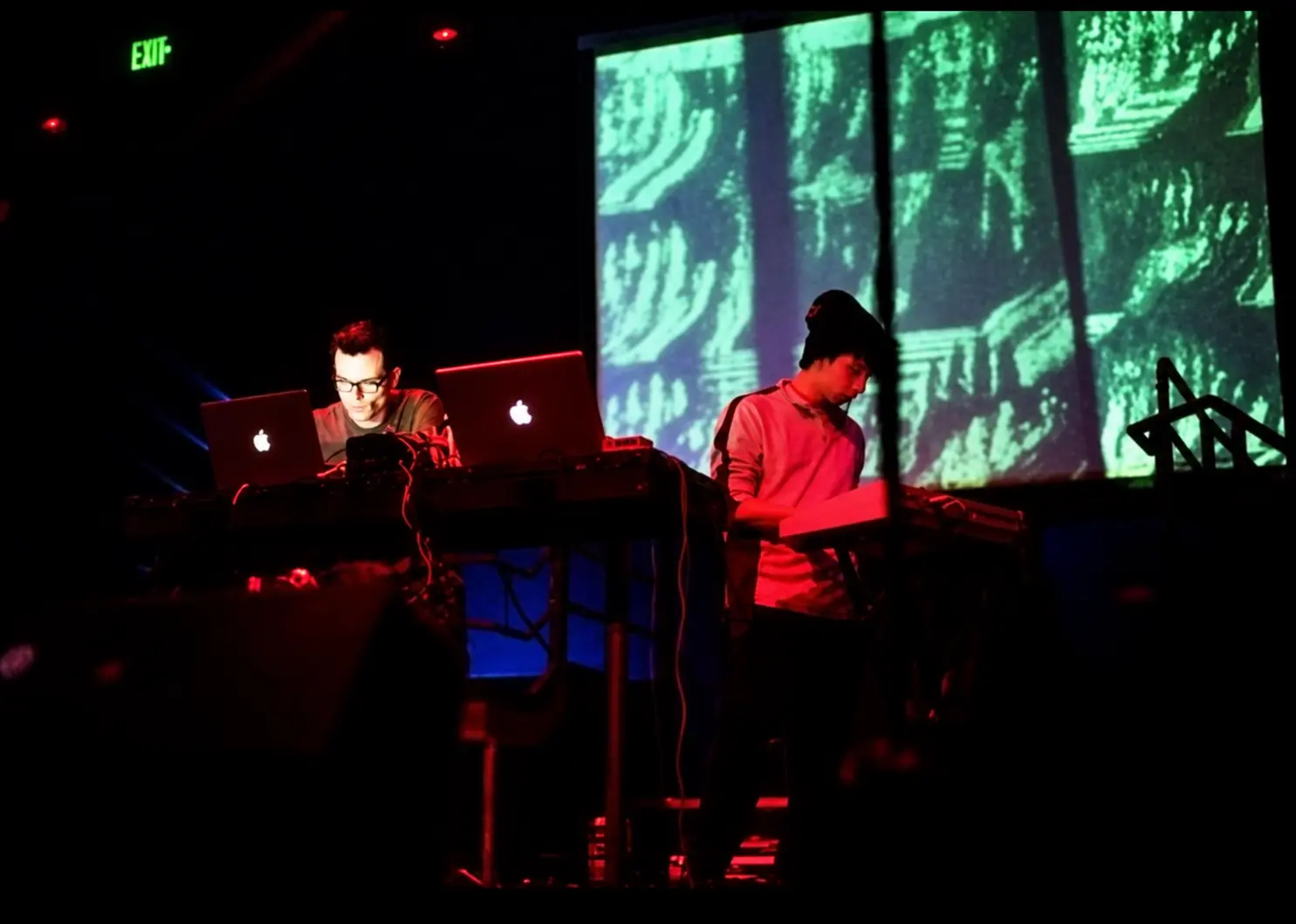 Cyrusrex and Squigg at their laptops on stage at DNA Lounge, San Francisco, green projections behind them