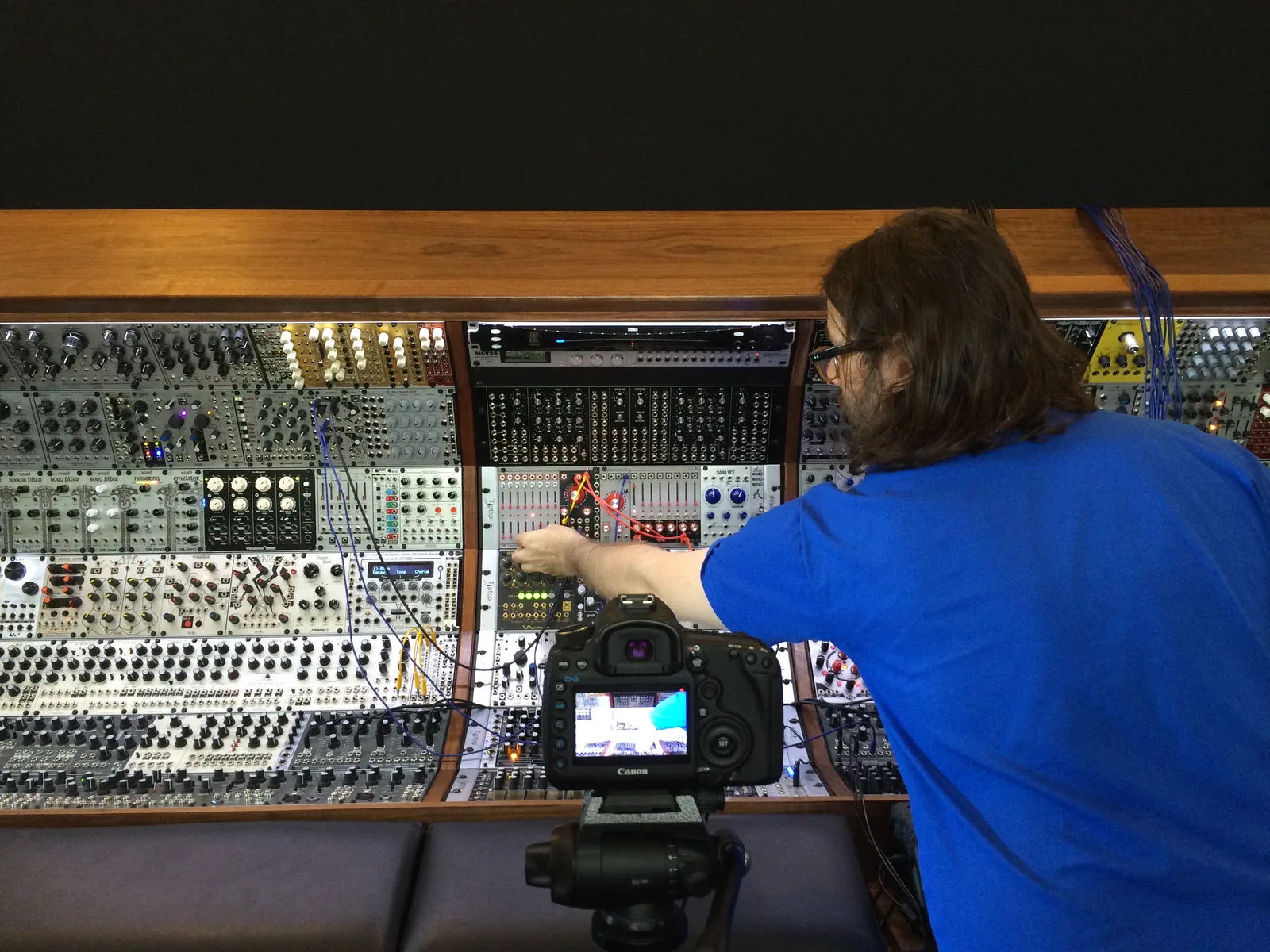 Alessandro Cortini reaching into the big modular, a camera on a tripod in front of him