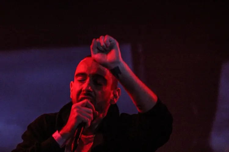 Jon Bates of Big Black Delta singing with a hand raised, lit red: Black Line live at the Teragram Ballroom