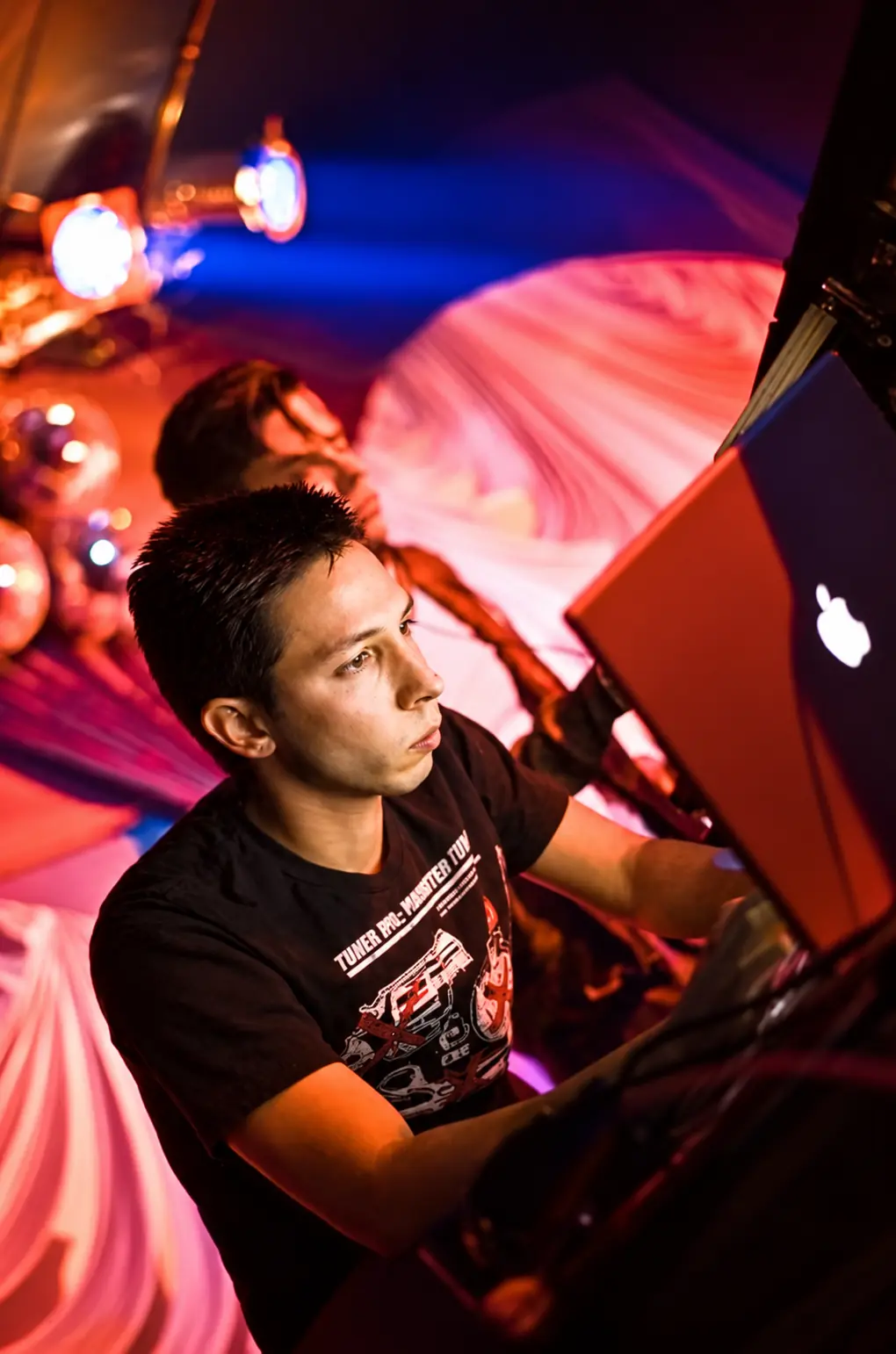 Cyrusrex at a laptop and his gear on stage in red light