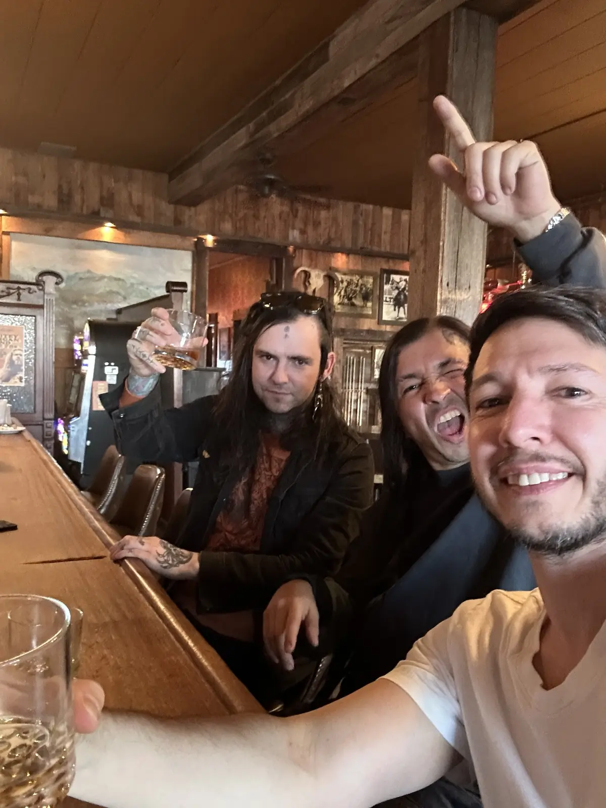 A selfie of three people at a wooden bar, one pointing up and one pulling a face