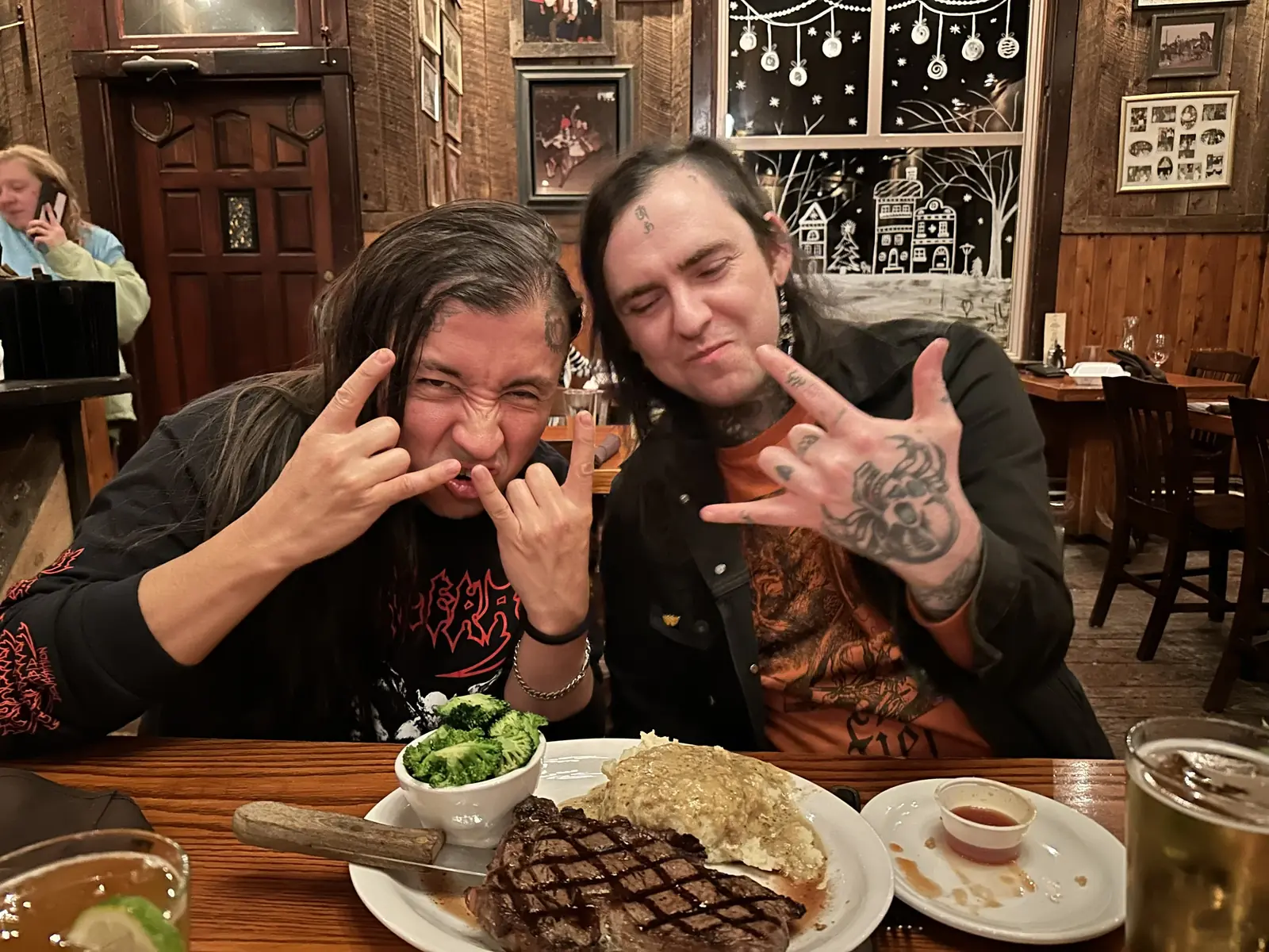 Two people throwing horns over a steak dinner in a wood-panelled restaurant