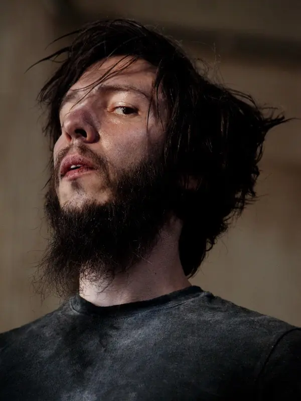 Cyrusrex from below, tousled dark hair and a beard, in warm light