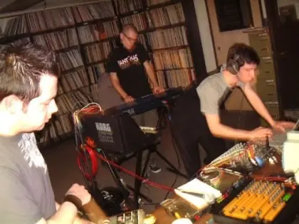 Cyrusrex live for KUCI: musicians with synths and a mixer in a room lined with records
