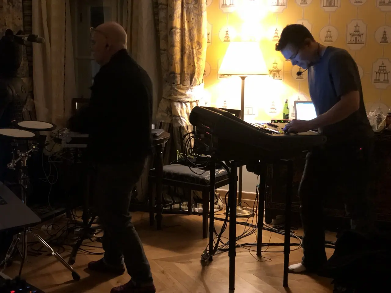 Black Line rehearsals at the hotel in Kraków: two men with keyboards and drum pads in a room with patterned wallpaper