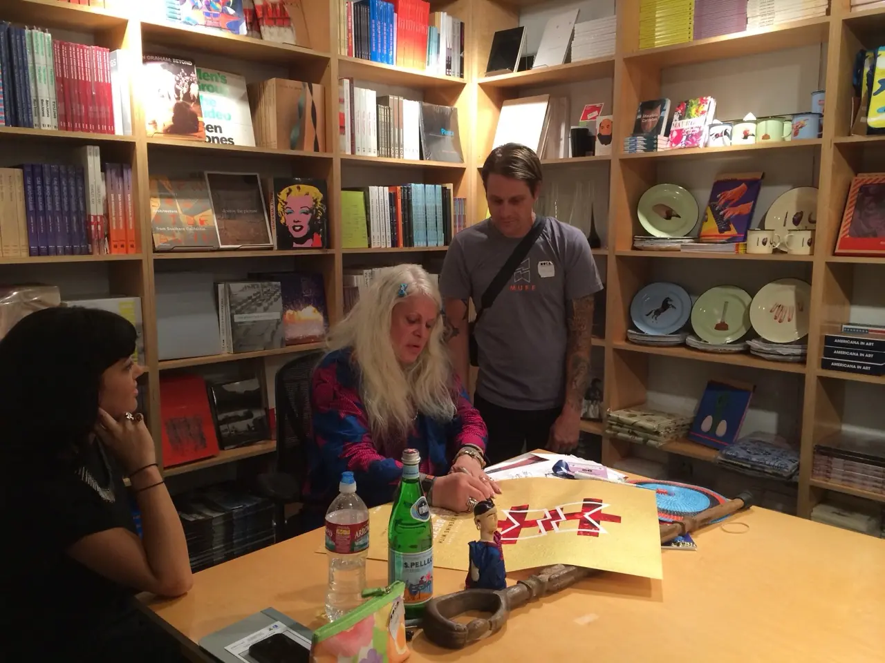 Genesis Breyer P-Orridge signing the MOCA posters at a table in a bookshop, Hazel Hill McCarthy III and Rodent beside her