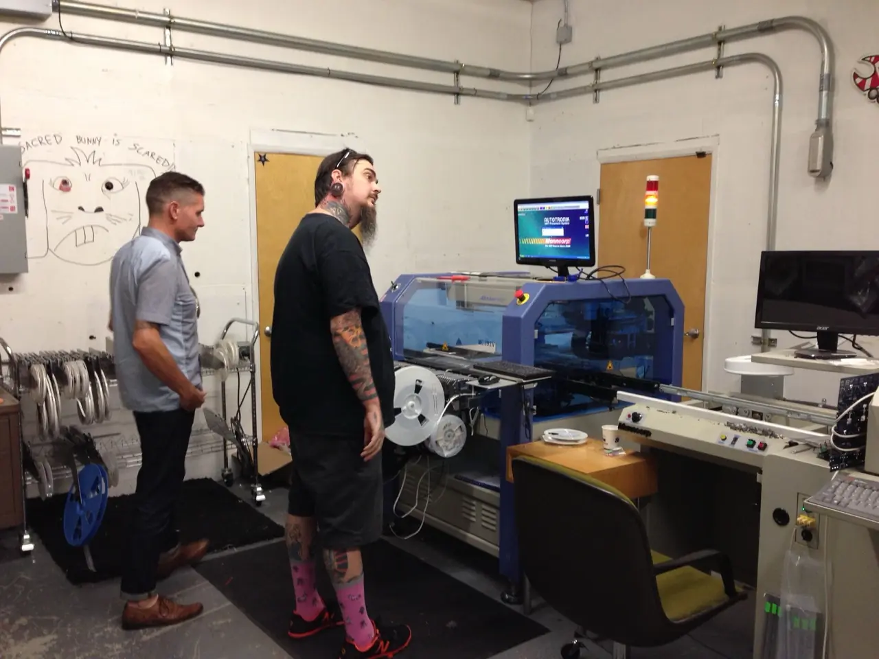 Josh and Douglas J. McCarthy by a surface-mount assembly machine on the production floor at DarkPlace Mfg.