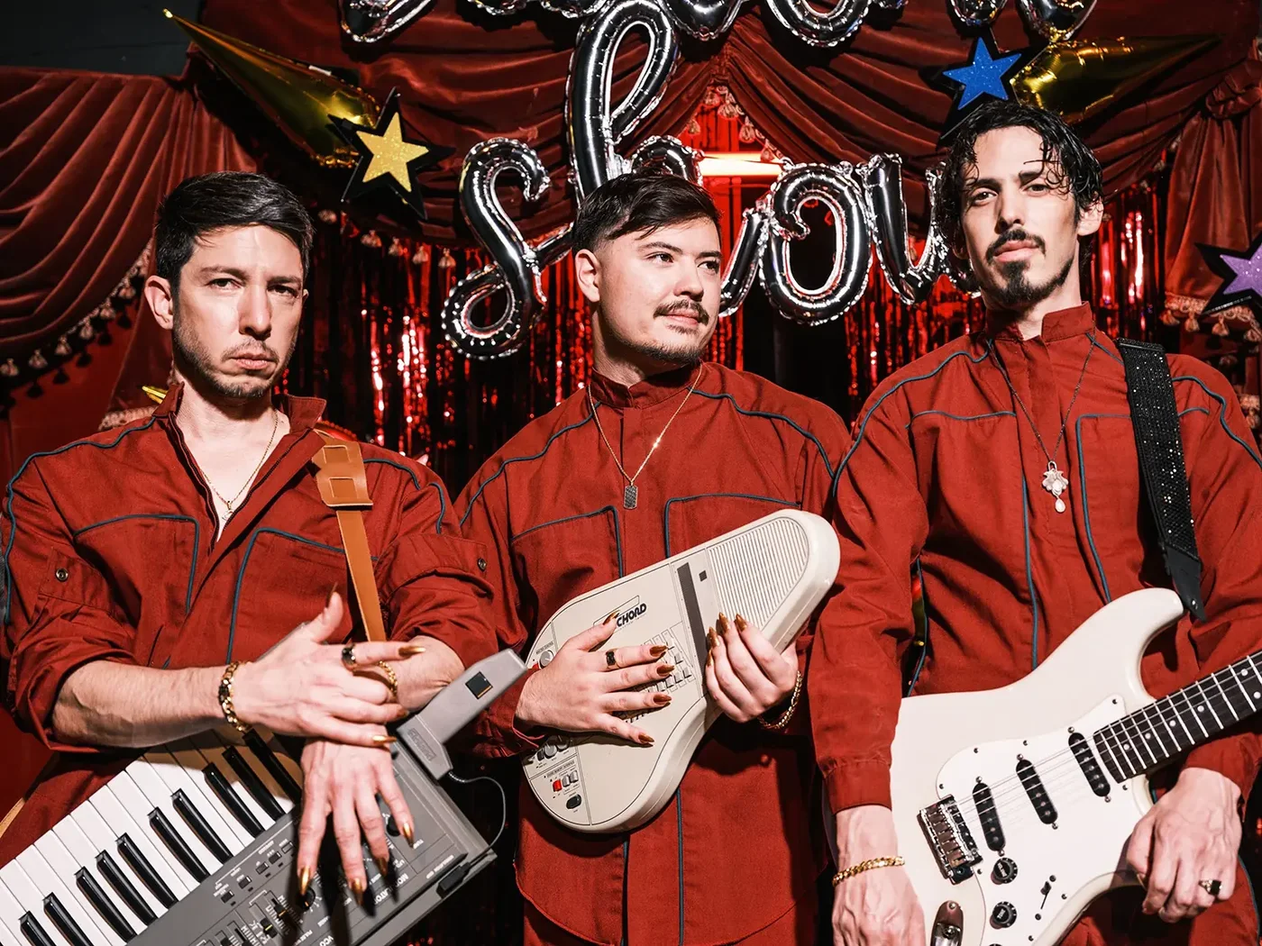 Talent Show: three musicians in red suits with a keytar and guitar in front of a theatre curtain