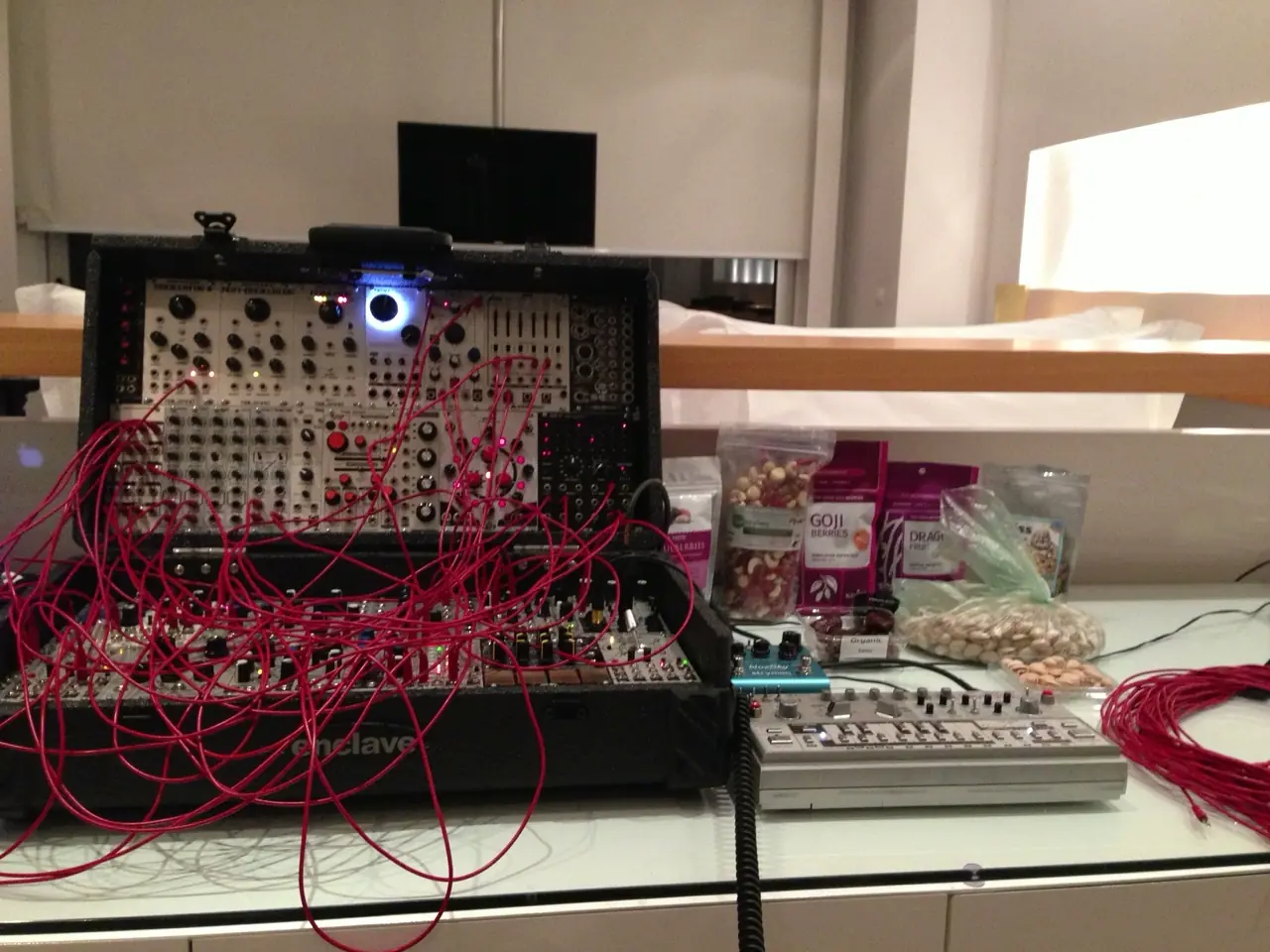 A suitcase modular patched with red cables beside two small silver machines