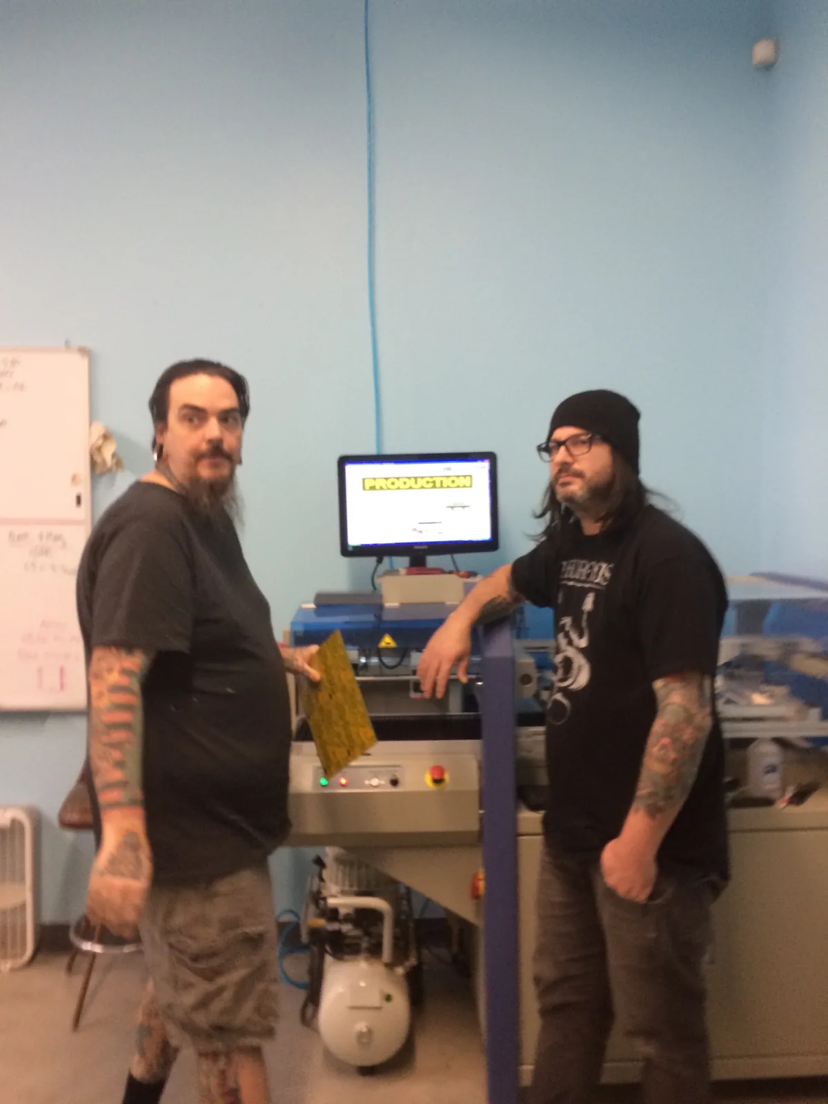 Two men beside a production machine at DarkPlace Mfg., its screen reading PRODUCTION