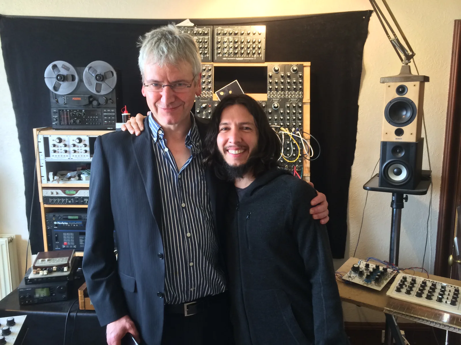 Ken MacBeth and Cyrus arm in arm in front of a modular system and tape machines