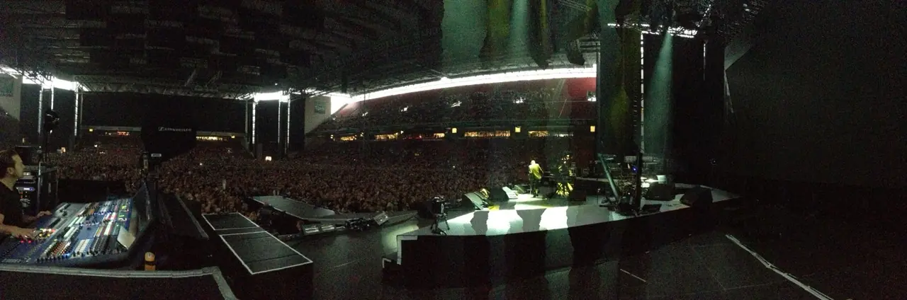 A packed arena during a show, seen from beside the mixing desk, the stage lit